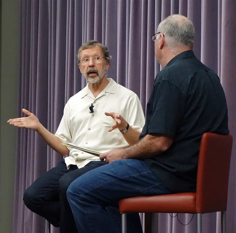 Edwin Catmull, seated on stage, talking with gestures in a conversation.