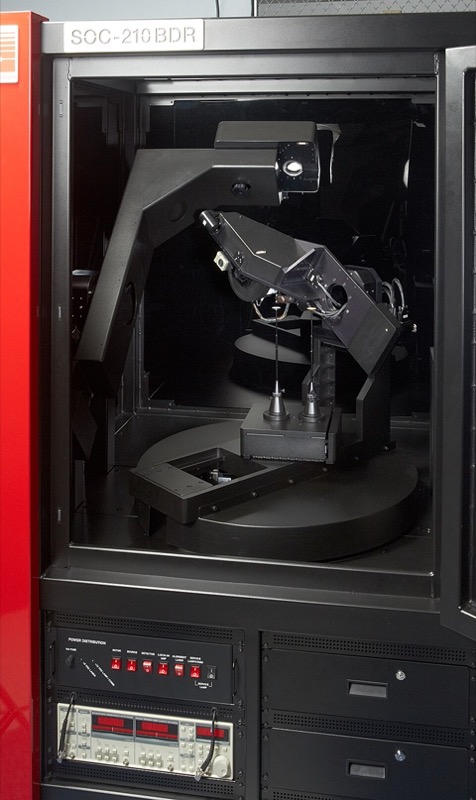 A commercial gonioreflectometer in an instrument cabinet: two articulated arms hold the light source and the detector over a rotating sample stage.
